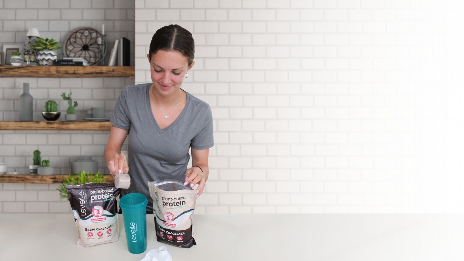Woman in a kitchen with protein powder containers and a tumbler.