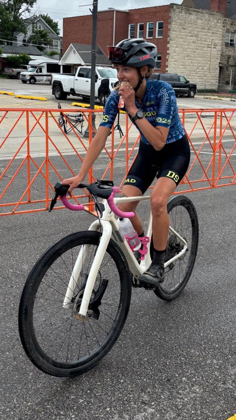 Person riding a bicycle on a street with orange barriers and buildings in the background