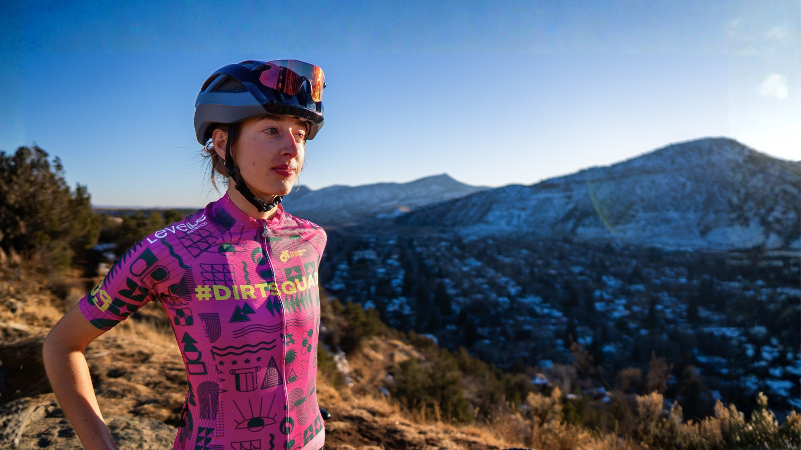 Person in a pink cycling outfit with a helmet standing on a mountain trail
