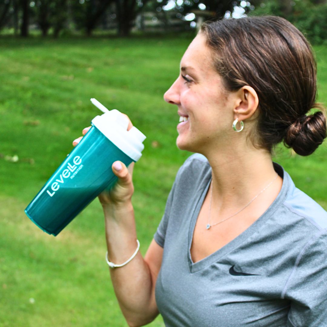 Woman holding a teal and white shaker bottle outdoors